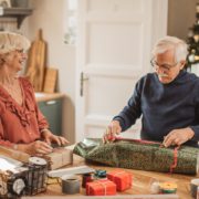 Couple wrapping holiday gifts at a table with good posture to prevent neck and back pain