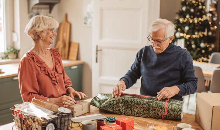 Couple wrapping holiday gifts at a table with good posture to prevent neck and back pain